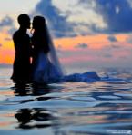 bride and groom standing thigh deep in a body of water at sunset